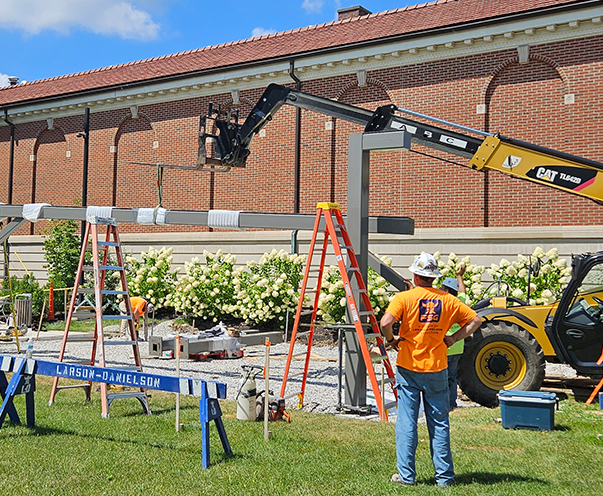 Facility Services Group workers watch as a steel beam is lowered into place