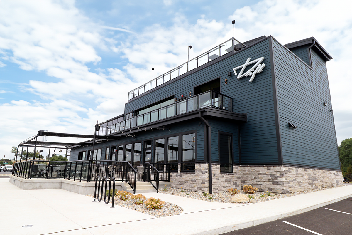 From Pine Lake, Drift on Pine features a spacious concrete patio with outdoor seating, a second-story balcony, and a rooftop lounge