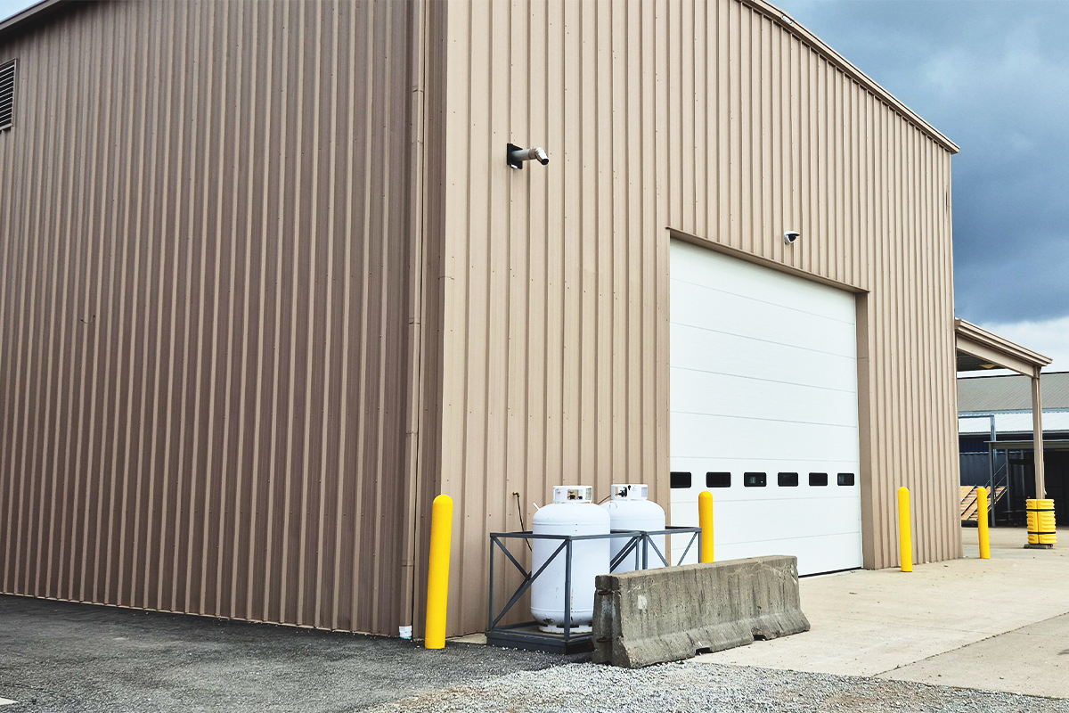 MAAC Tactical Building is a light tan pre-engineered metal building with a large drive-in door on the west side of the facility