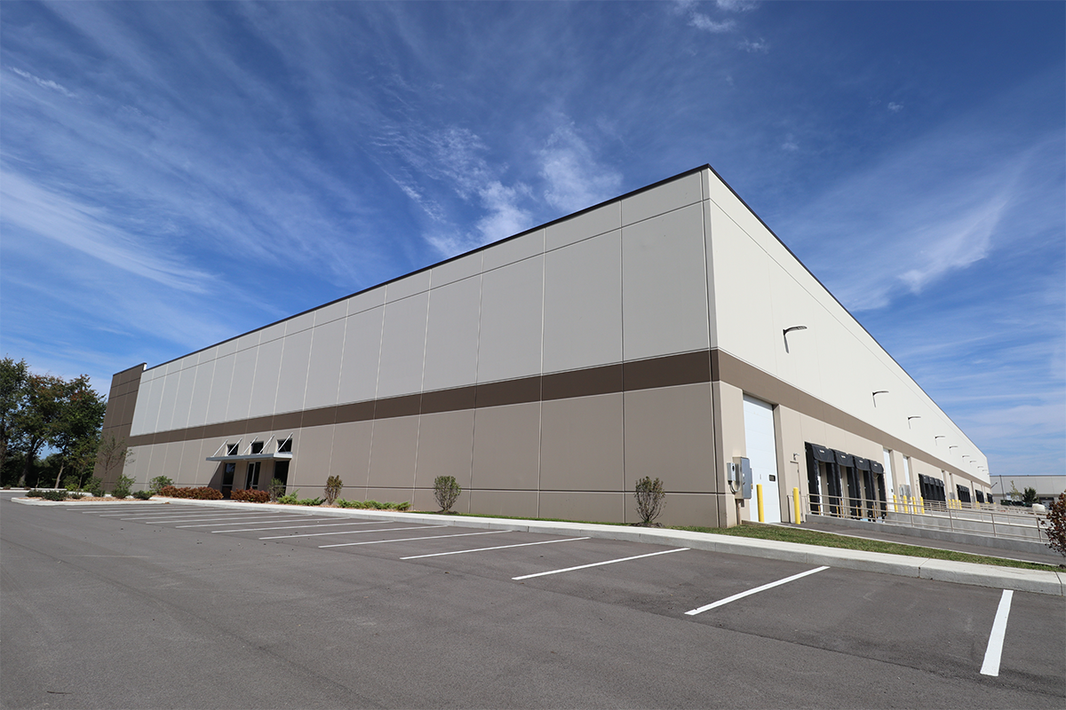A large industrial building sits in front of a asphalt parking lot with a blue sky shining in the background